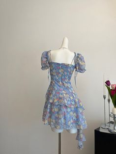 Circuitous and crafted with care, this blue floral dress weaves its way through timeless fashion with a modern twist. The layers of lightweight fabric create a gentle cascade, giving this dress a buoyant, ethereal quality that’s perfect for spring and summer events. Decorated with a vibrant array of floral patterns in soft hues, the dress features dainty shoulder straps and a rosette detail for a touch of romance. Its asymmetrical hemline and flowing silhouette ensure it moves gracefully with th Cascade Dress, Floral Cascade, Blue Floral Dress, Old Hollywood Glamour, Floral Blue Dress, Summer Events, Classic Films, Flared Skirt, Hollywood Glamour