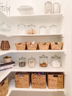 an organized pantry with wicker baskets and glass jars on the shelves, all white