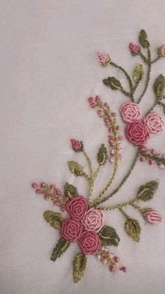 a white vase filled with pink flowers on top of a table next to a wall