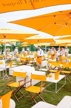 many tables and chairs with yellow umbrellas in the grass at an outdoor function venue