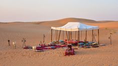 a tent set up in the desert with pillows and blankets on it's sides