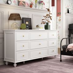 a white dresser sitting next to a bed in a room with floral wall paper on the walls