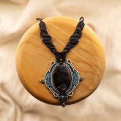 a wooden box with a beaded necklace on it's side and a black stone in the middle