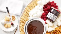 a platter filled with marshmallows, pretzels, raspberries and other snacks