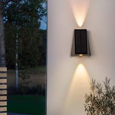 two lights on the side of a white wall next to a potted plant and chair