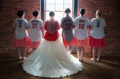 a group of women standing next to each other in front of a brick wall wearing baseball uniforms