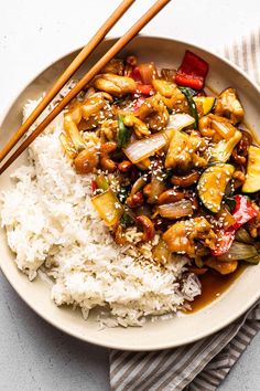 a white bowl filled with rice and vegetables next to chopsticks on the side