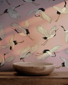 a bowl sitting on top of a wooden table next to a wall with birds painted on it