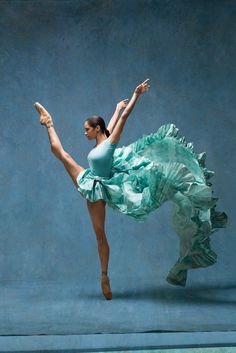 a woman in a green dress is dancing with her arms outstretched and legs spread out