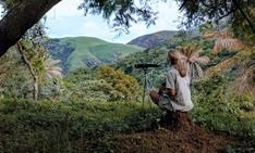 a woman sitting on top of a dirt hill next to a forest filled with trees