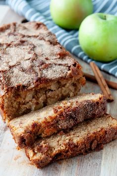 two pieces of bread sitting on top of a wooden cutting board next to green apples