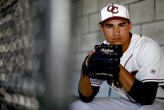 a baseball player holding a catchers mitt in front of a brick wall and chain link fence