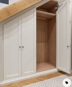 an open cabinet in the corner of a room with white walls and wood flooring