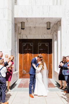 a bride and groom are kissing in front of the doors of a building with confetti thrown around them