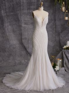 a white wedding dress on display in front of a gray backdrop with flowers and greenery