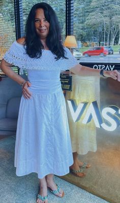 a woman in a white dress standing next to a window with the words vas on it