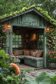 a garden shed with lots of flowers growing on the roof and windows, sitting next to a wooden deck