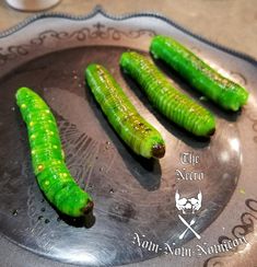 four green pickles sitting on top of a metal plate next to a glass cup