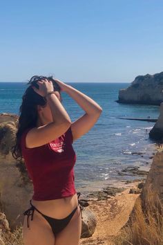 a woman in a red top and black panties standing on the beach looking at the ocean