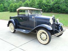 an old model car parked in front of some bushes