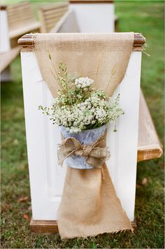 an old chair with burlock tied to it and flowers in the vase on top