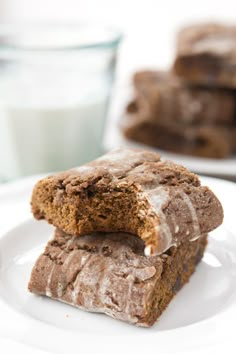 two pieces of brownie on a white plate with a glass of milk in the background