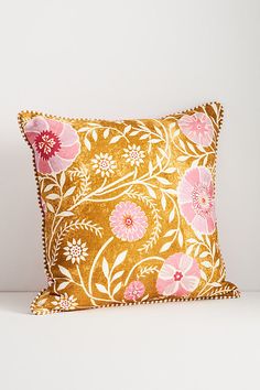 a yellow and pink floral pillow sitting on top of a white table next to a wall