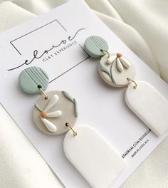 two white and green earrings on top of a piece of paper next to a card