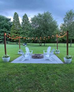 an outdoor fire pit surrounded by lawn chairs and potted plants with lights strung over it