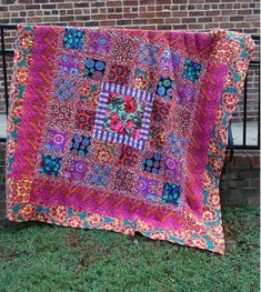 a pink and blue quilt is hanging on a black iron fence in front of a brick wall