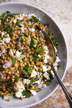 a white bowl filled with lots of food on top of a wooden table next to a metal spoon