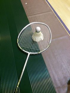 a badminton racket with a ball on it sitting on the floor next to a court