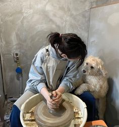 a woman sitting on top of a pottery wheel next to a dog