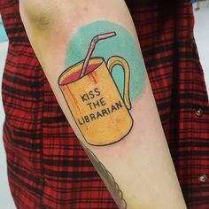 a person with a tattoo on their arm has a mug that says kiss the librarian