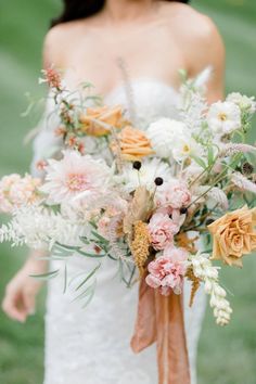 a bride holding a bouquet of flowers in her hand and wearing a white dress with an orange sash