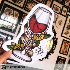 a person holding up a sticker with a wine glass on it in front of a wall full of pictures