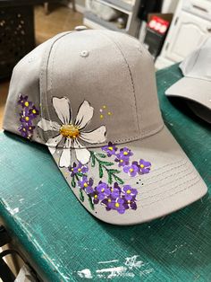 a hat with flowers painted on it sitting on top of a green table next to other hats