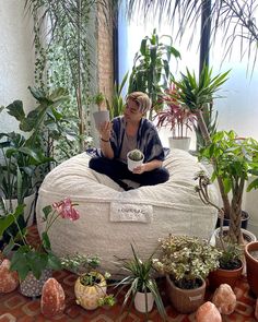 a woman is sitting on a bean bag chair surrounded by potted plants and holding a coffee cup