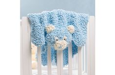 a crocheted teddy bear blanket hanging from the side of a baby crib