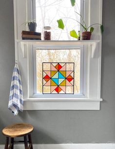 a stained glass window in the corner of a room with a stool and potted plants