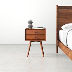 a bed and nightstand in a room with a white wall behind the bed, one end table has a lamp on it