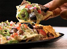 a hand holding a tortilla over a plate full of nachos and vegetables