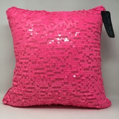 a pink sequin pillow with a black tag hanging from the side on a gray background