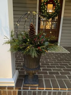 a potted plant with pine cones and greenery sits on the front steps of a house