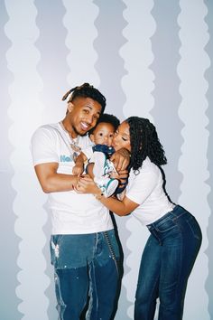 a man and woman holding a baby in front of a wall with wavy lines on it