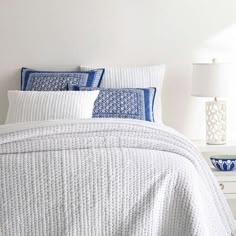 a white bed with blue and white pillows on top of it next to a night stand