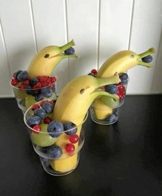 two cups filled with fruit and bananas on top of a black table next to a white wall