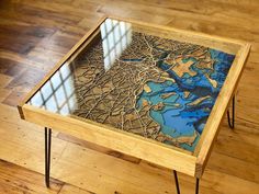 a wooden table with a glass top sitting on a hard wood floor next to a window