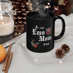 a black coffee mug sitting on top of a table next to candles and pine cones