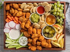 a platter filled with chicken, waffles, grapes, celery, carrots and crackers